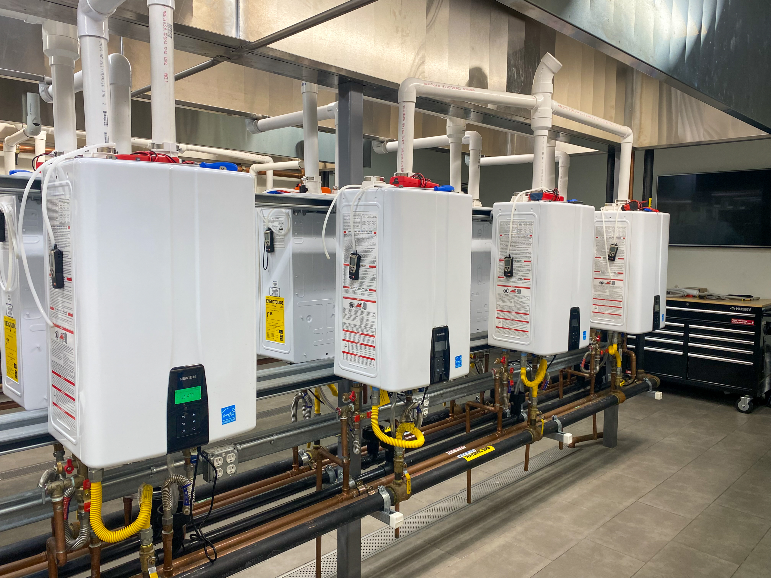 A row of tankless water heaters are installed in a commercial plumbing setting.