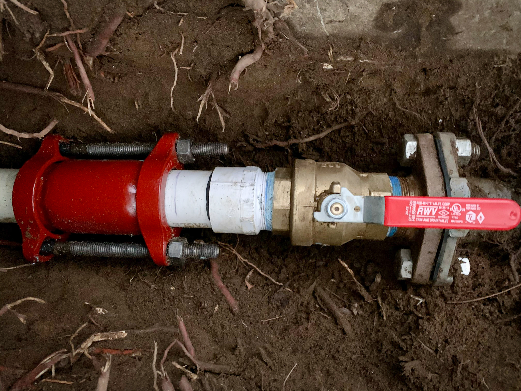 A Valley Center plumber's water main repair, utilizing a red mechanical coupling and brass ball valve.
