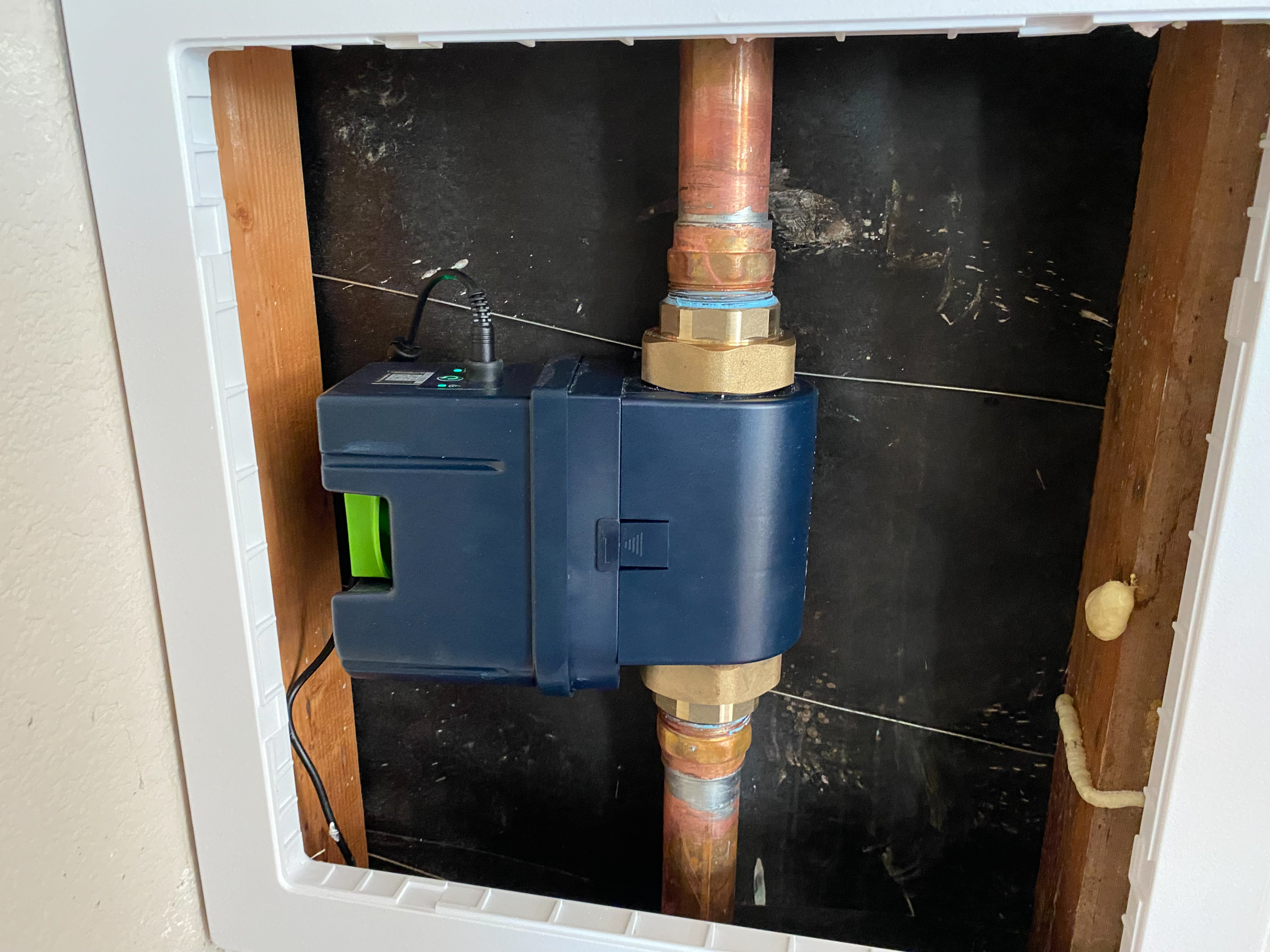 A Moen Flo Smart Water Monitor is installed in a garage with an access panel to prevent leaks and plumbing repairs.