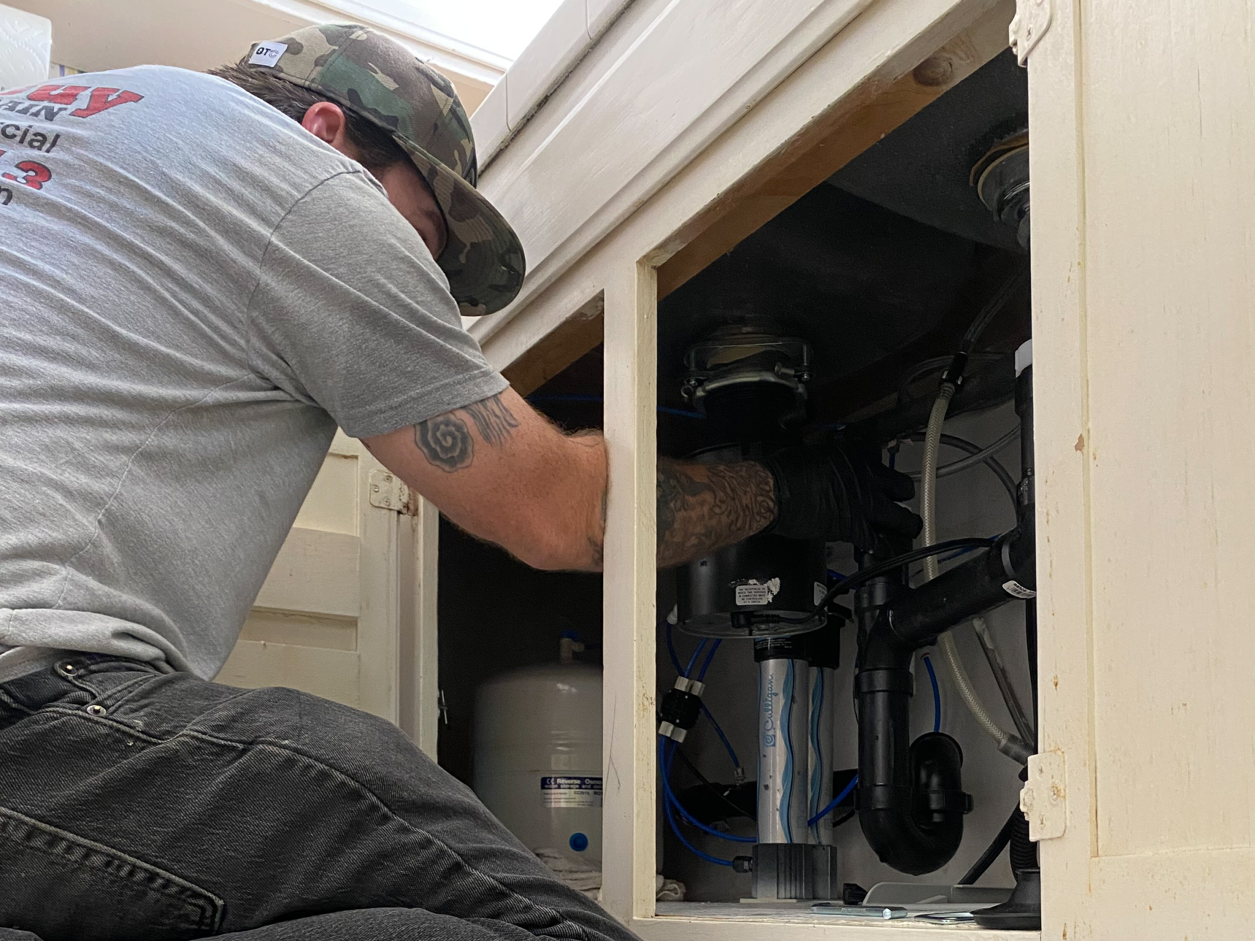 A plumber inspects the plumbing beneath a kitchen sink to ensure there are no leaks or other concerns.