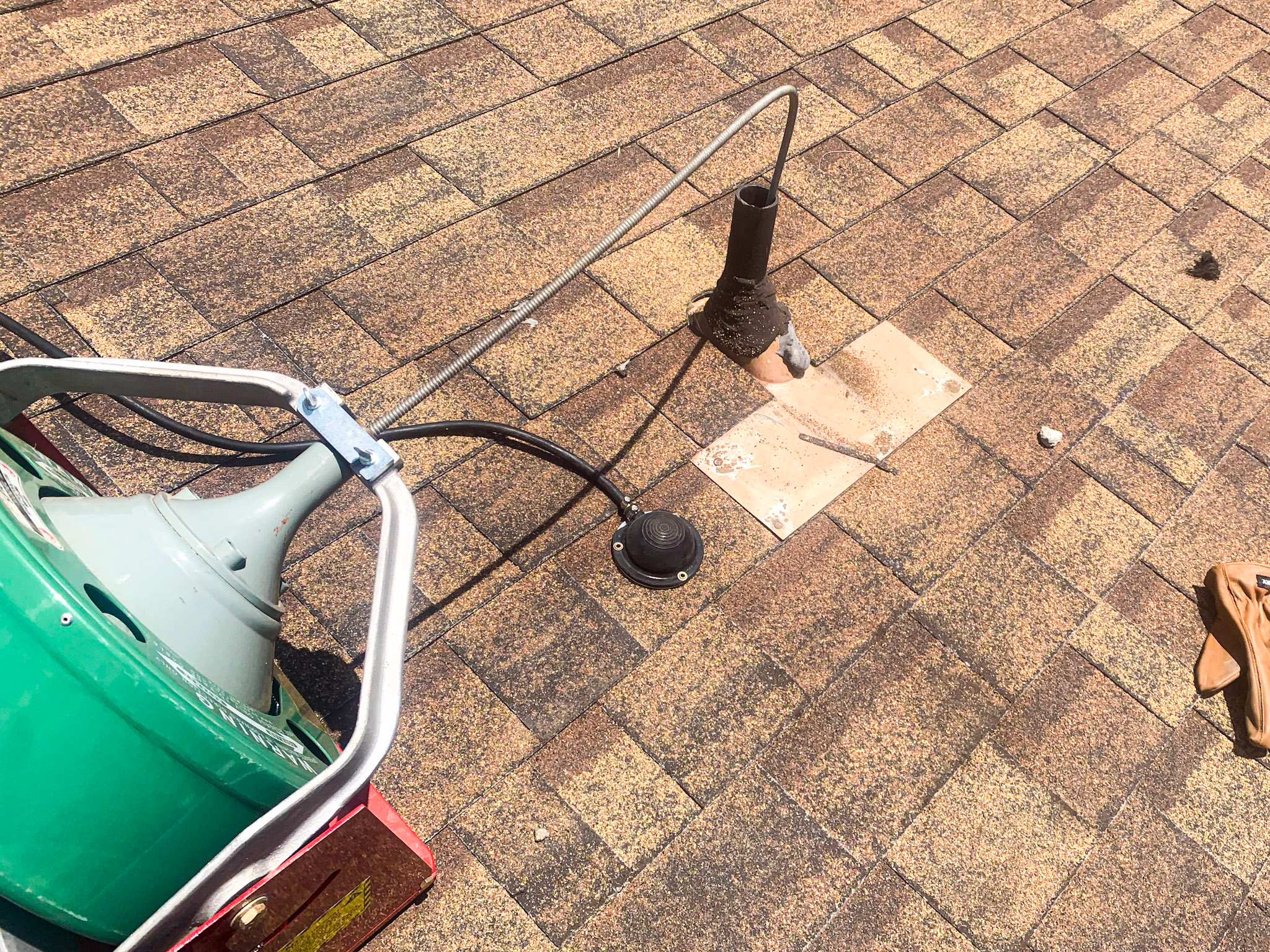 Professional drain cleaning service is performed from a roof top, using the drain vent for access.