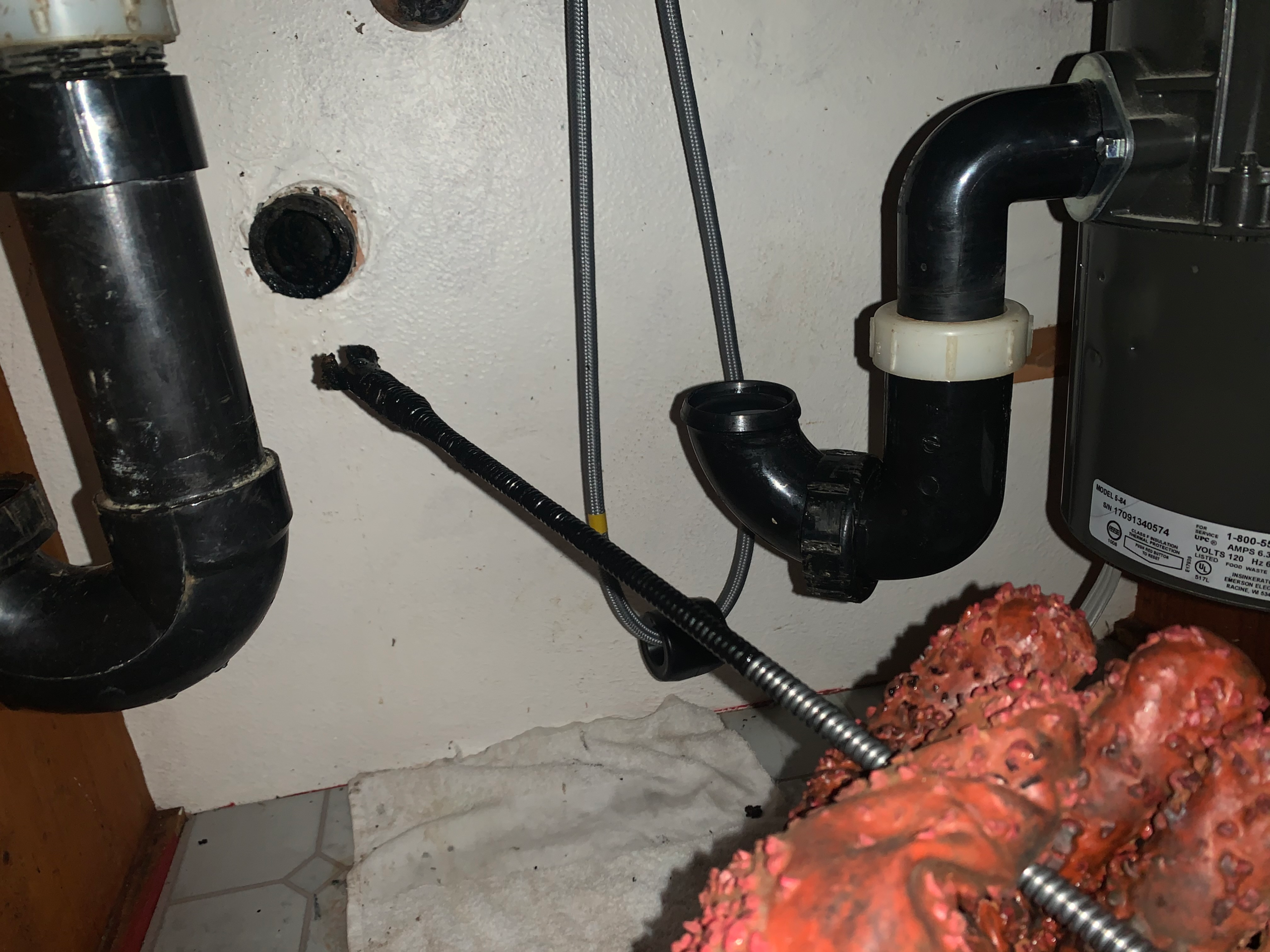 A plumber removes grease residue from a kitchen sink drain using a drain snake.